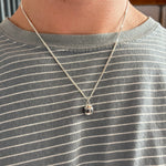 A silver chain necklace with a small cocktail can pendant featuring the word 'BuzzBallz' printed in bold black letters, shown on a mans neck.