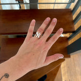 A silver NY Yankees logo ring worn on a person's ring finger, shown in a lifestyle setting with wooden stairs in the background.